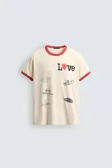 Camiseta de manga corta color crema con cuello redondo y ribetes en color rojo. Presenta un estampado frontal con la palabra "Love" donde la 'o' es un corazón rojo, y varios parches gráficos en tonos grises y negros.