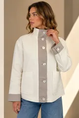 Campera de lino color crudo, con detalles en gris topo en la solapa de los botones, cuello alto y puños. Cuenta con bolsillos frontales aplicados, botones de nácar y silueta amplia.