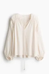 Blusa oversized de viscosa color beige con escote en V pronunciado, cordones ajustables con cuentas en los extremos, hombros caídos y mangas globo largas con puños elásticos.