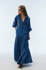 Camisa oversize blanca de lino, con corte cuadrado, mangas raglán cortas con puños anchos, aberturas laterales y cierre frontal de botones.