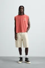 Camiseta tank cropped fit color ladrillo, con cuello redondo y sisa. Estampado frontal y trasero con gráficos y textos en color amarillo. Efecto lavado.