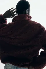 Buzo de sherpa con textura de borrego, color bordó, de corte oversized y hombros caídos. Presenta cuello elevado con medio cierre frontal, bolsillos laterales insertados y canesú en frente y espalda.