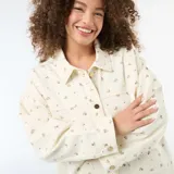 Sobrecamisa de twill color blanco con estampado floreado sutil, corte holgado, cuello camisero, cierre frontal con botones metálicos y dos bolsillos de parche delanteros.