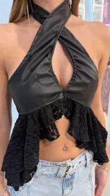 Top negro de cuerina con escote halter cruzado, abertura frontal en el pecho y detalle de volados de encaje en el ruedo.