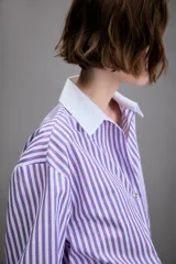 Camisa de manga larga con cuello solapa y puños en contraste color blanco. Presenta un diseño de rayas verticales en color lila y blanco, con cierre frontal de botones.