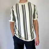 Remera de tejido de punto en hilo de algodón, con diseño de rayas verticales en tonos blanco, beige y gris oscuro. Presenta cuello redondo y mangas cortas con terminaciones acanaladas, de corte semi oversize.