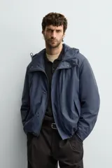 Parka de tejido técnico con acabado engomado, cuello subido y capucha ajustable. Presenta cierre frontal con cremallera oculta bajo solapa con botones a presión, bolsillos laterales de vivo y mangas largas con puños ajustables.
