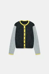 Chaqueta de punto con diseño color block, cuello redondo y manga larga. Presenta cuerpo en color gris oscuro, mangas en gris claro y detalles de ribetes en color amarillo vibrante. Cierre frontal con botones oscuros.