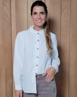 Camisa blanca de algodón con cuello alto tipo mao y volados sutiles a lo largo de la botonadura frontal. Presenta mangas largas con frunces en los hombros y botones frontales.