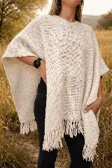 Poncho tejido en lana merino de color crudo, con diseño de punto grueso y terminación de flecos en el ruedo.