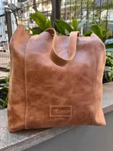 Bolso tipo shopper de cuero con acabado texturizado en tono metalizado claro. Cuenta con doble asa de hombro y etiqueta de cuero con logo grabado en la parte inferior frontal.