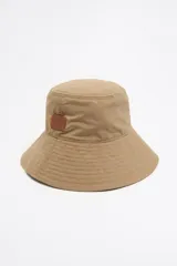 Gorro tipo bucket color beige de gabardina con etiqueta de cuero con logo de la marca.