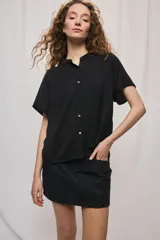 Camisa negra de manga corta, silueta amplia y tejido liviano con textura. Presenta cuello mao, cierre frontal con botones y diseño fluido.