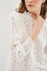 Camisa negra de algodón con cuello alto, cierre frontal de botones y detalles de encaje vertical y en los puños.