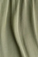 Vestido corto verde oliva con leve brillo, cuello halter elevado con frunces, cuerpo holgado con cintura elástica y falda corta de corte asimétrico.