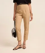 Pantalón de sastrería corte carrot, color beige, con cintura alta, pinzas frontales y cinturón fino incorporado con hebilla metálica.