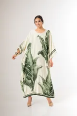 Maxi túnica oversize de tela con acabado nacarado, cuello redondo, mangas amplias y bolsillos laterales, con estampa de hojas de palmera en negro sobre fondo blanco.