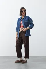Sobrecamisa de jean color negro con silueta relajada, cuello camisero, cierre frontal con botones metálicos, bolsillos frontales y cinturón ajustable en la cintura.