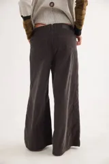 Pantalón sastrero de tiro medio confeccionado en pana de algodón. Presenta un diseño de pierna ancha con costuras verticales decorativas, bolsillos delanteros y traseros, y un detalle de aplique con ojalillo metálico en el ruedo de una de las piernas.