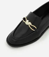 Zapato mocasín femenino de PU color negro, con punta cuadrada y detalle metálico dorado en el empeine. Tiene un tacón bajo y suela de goma.