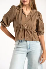 Blusa blanca de algodón con delicado bordado floral, mangas abullonadas de largo 3/4 y cierre frontal con botones y cordón ajustable en la cintura.