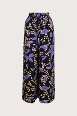 Pantalón de pierna ancha con estampado de hojas y manchas en tonos morado y beige sobre fondo negro. Cuenta con cintura elástica ajustable con cordón y aberturas laterales.