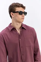 Camisa de manga larga color borravino, de tejido rústico de algodón con textura natural, cuello clásico, botones frontales y un bolsillo aplicado en el pecho.