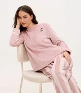 Pijama de dos piezas confeccionado en tejido fleece de tacto suave. La blusa es de cuello redondo y manga larga, con un pequeño bordado de flor en el pecho. El pantalón presenta un diseño de rayas verticales y cintura elástica.