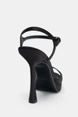 Sandalia de tacón fino alto y plataforma, confeccionada en tela satinada color negro. Cuenta con una tira delantera y cierre mediante tira con hebilla en el tobillo.