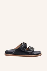 Sandalias de cuero color negro con dos tiras anchas sobre el empeine, cada una con hebillas metálicas ajustables y detalles de tachas plateadas. La suela es de cuero con un borde de color madera.