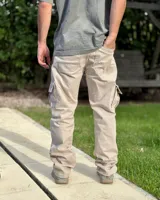 Pantalón cargo de corte holgado, color arena, confeccionado en gabardina elastizada. Presenta bolsillos laterales con solapa en los muslos, costuras reforzadas en las rodillas y cierre frontal con botón y cremallera.