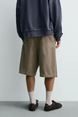 Bermuda wide fit color beige, confeccionada en pana de algodón. Presenta pliegues frontales en la cintura, bolsillos delanteros y bolsillos traseros de plastrón. Cierre frontal con cremallera y botón.