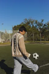 Buzo de punto tejido en jacquard con diseño de rayas verticales en tonos beige y blanco. Presenta cuello polo en color negro, puños y ruedo acanalados en blanco, y bordados alusivos al mundial en el pecho.