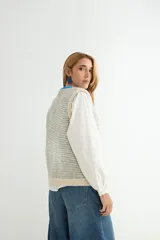 Chaleco de punto con diseño a rayas horizontales en gris y blanco. Presenta cuello redondo, bordes y bolsillos frontales con detalles en color rojo, y cierre frontal con botones rojos.