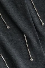 Vestido corto de punto color gris oscuro, con diseño cruzado, escote en V y aplicación de tiras de strass colgantes en el frente. Cuenta con mangas largas y hombreras.