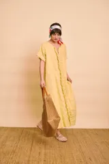 Vestido tipo túnica largo de lino color amarillo, de manga corta, con bolsillos laterales y detalle de volados en la botonera frontal.