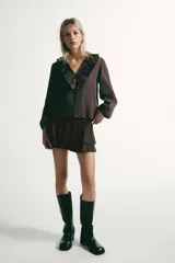 Camisa de manga larga con estampado de cuadros, escote en pico con volantes decorativos y cierre frontal con botones. Presenta puños elásticos.