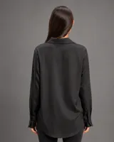 Camisa de satén color negro, de manga larga con puños clásicos, cuello camisero y cierre frontal con botones al tono. Presenta un corte recto y acabado brillante.