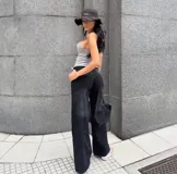 Pantalón de denim rígido negro, tiro alto, de corte ancho (wide leg) y largo. Presenta costuras visibles en el frente que simulan un diseño de paneles.