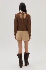 Sweater marrón de tejido de lurex con mezcla de puntos y flecos en el frente. Cuenta con escote abierto en la espalda y lazo.