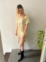 Vestido corto dorado de lentejuelas con escote en V, mangas cortas y flecos en el ruedo.