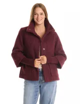 Tapado de tejido bouclé color marrón, con silueta evasé y largo a la cadera. Presenta cuello alto envolvente, cierre frontal oculto con botones a presión y bolsillos frontales de gran tamaño. Sus mangas son 3/4 con corte amplio y puños de tejido rib al tono que se extienden para cubrir las muñecas.