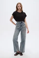 Pantalón jean de tiro alto y corte ancho, con diseño estampado de pedrería y tachas en la parte frontal.