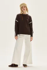 Sweater de tejido de punto color beige, con cuello redondo y detalles de bordado en zigzag en color azul oscuro a lo largo de las mangas y hombros. Presenta un pequeño bordado con texto en el pecho.