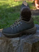Calzado tipo bota de trekking color verde oliva, con cordones al tono y suela de goma dentada en color marrón. Presenta un diseño robusto con refuerzos laterales y detalles metálicos en los ojales.