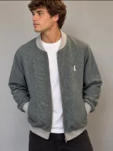 Campera bomber verde con patrón de espigas, confeccionada en paño fino. Cuenta con cierre frontal y detalles de rib en color gris en cuello, puños y cintura. Presenta un pequeño bordado blanco en el pecho.