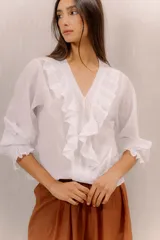 Camisa blanca de algodón con escote en V, volados delanteros con detalles de encaje y mangas largas con puños fruncidos.