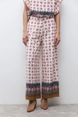 Pantalón de corte recto y tiro alto con estampado geométrico en tonos rojos y negros sobre fondo crudo. Presenta un borde inferior con diseño ornamental y bolsillos laterales.