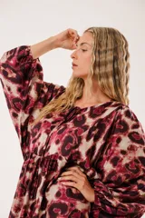 Vestido midi con estampado animal print en tonos borgoña y beige, con escote redondo y abertura en el pecho que se ajusta con lazos finos. De silueta relajada, manga larga tipo globo con terminación fruncida y falda amplia con recortes.