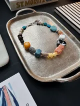 Collar corto de diseño multicolor, compuesto por cuentas grandes y medianas de diversas formas, texturas, tamaños y materiales, incluyendo cuentas de piedra, cerámica y resina en tonos turquesa, mostaza, marrón, blanco, negro y coral.